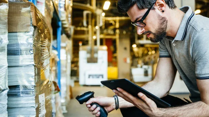 Man holds handheld scanner while reading his tablet.