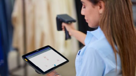 Woman looks at tablet screen while using handheld scanner.