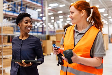 A read haired employee talks to a woman in a black shirt, both hold handheld devices using CheckMy.