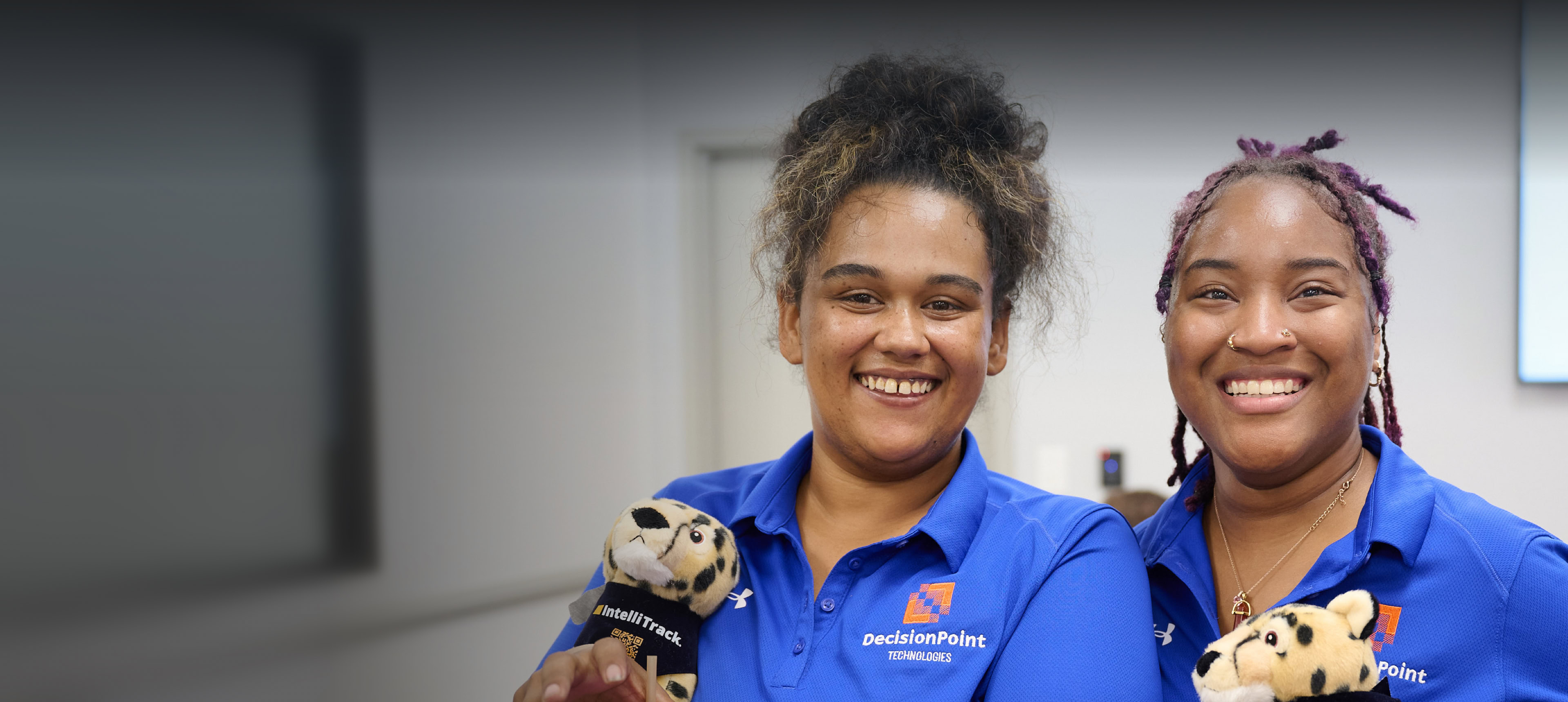 Two DecisionPoint employees smile in their blue shirts, holding IntelliTrack stuffies.