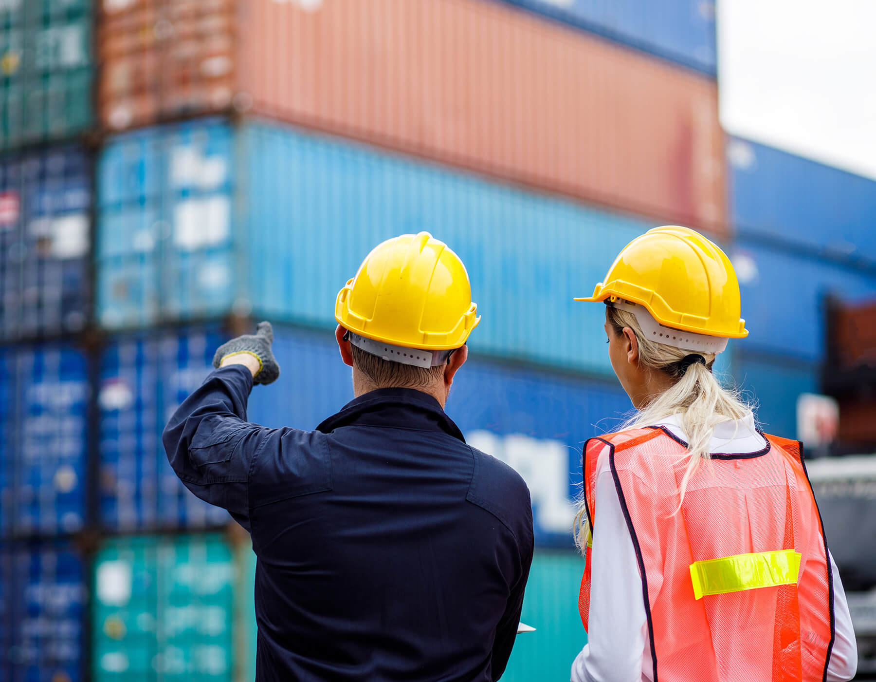 Two people in yellow hardhats discuss frontline worker enablement tools while looking at shipping containers.