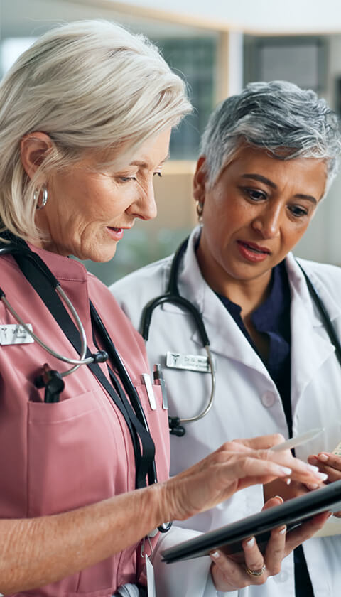 Two healthcare specialists check patient charts on a mobile device.