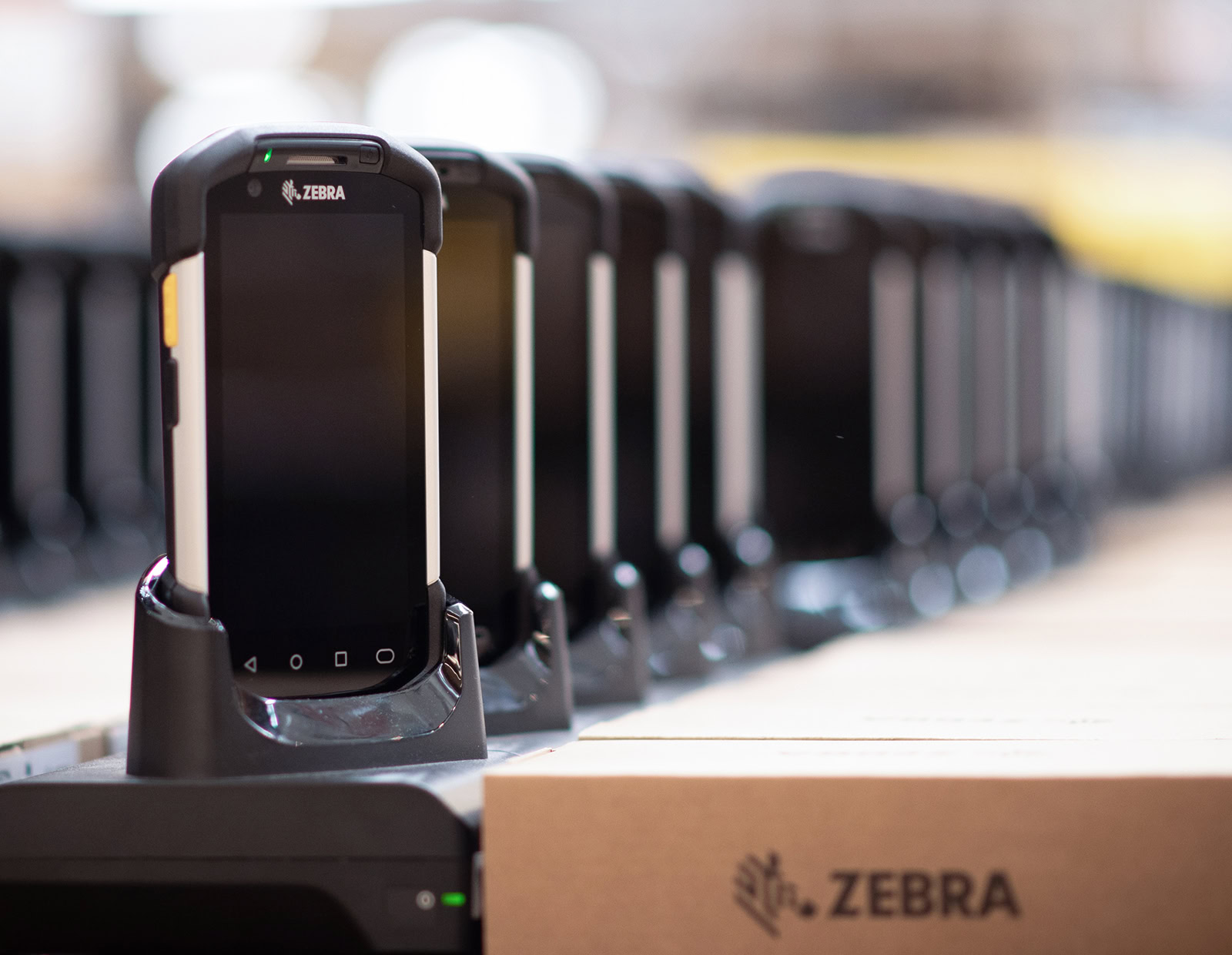 Zebra devices in a row on chargers, preparing for deployment to a device rental customer.