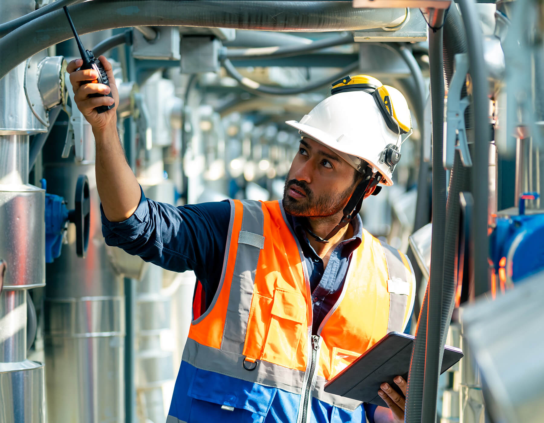 Employee in PPE uses devices including CheckMy software, holding a walkie talking and a tablet.