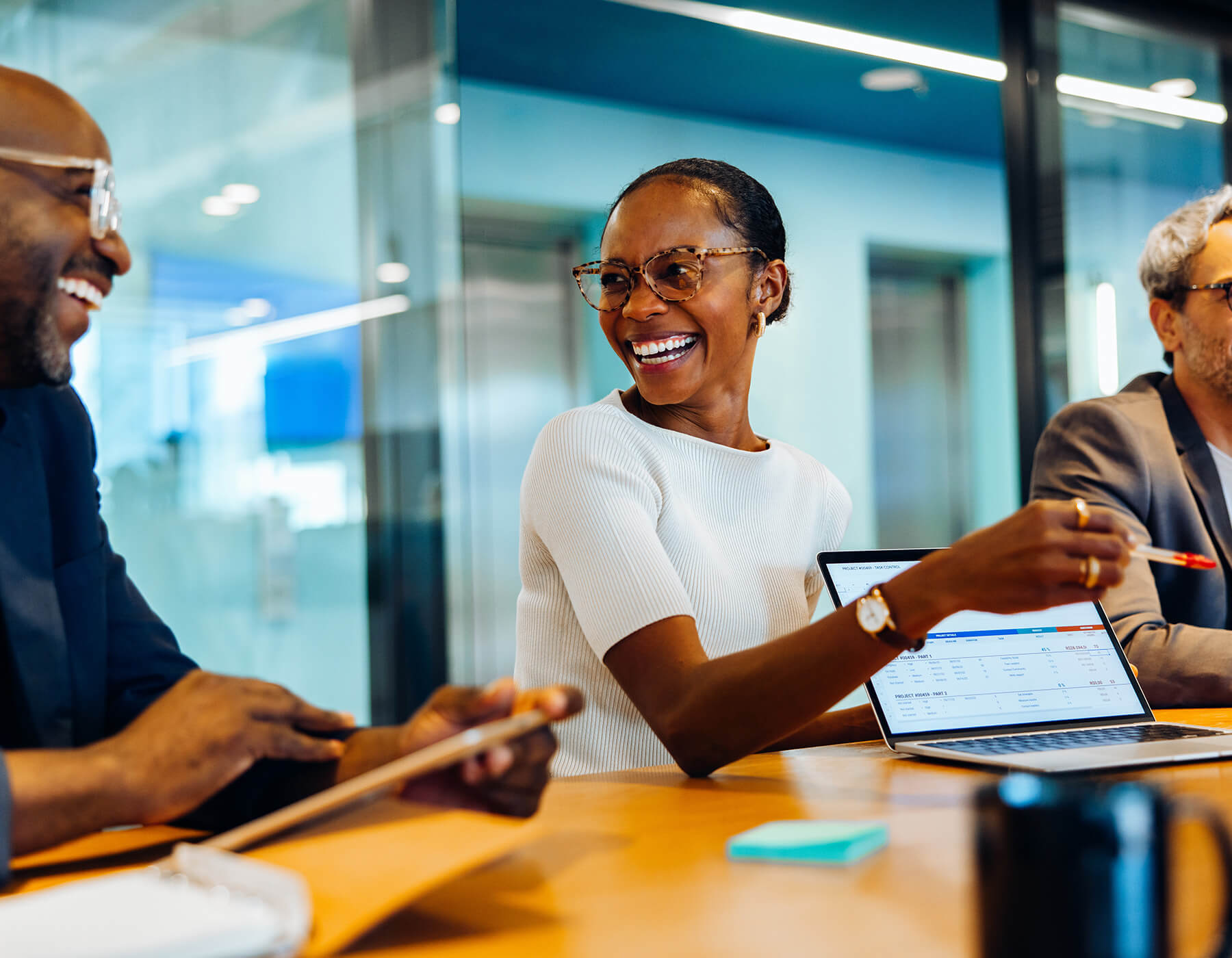 Woman smiles while showing data on her laptop in a board room.