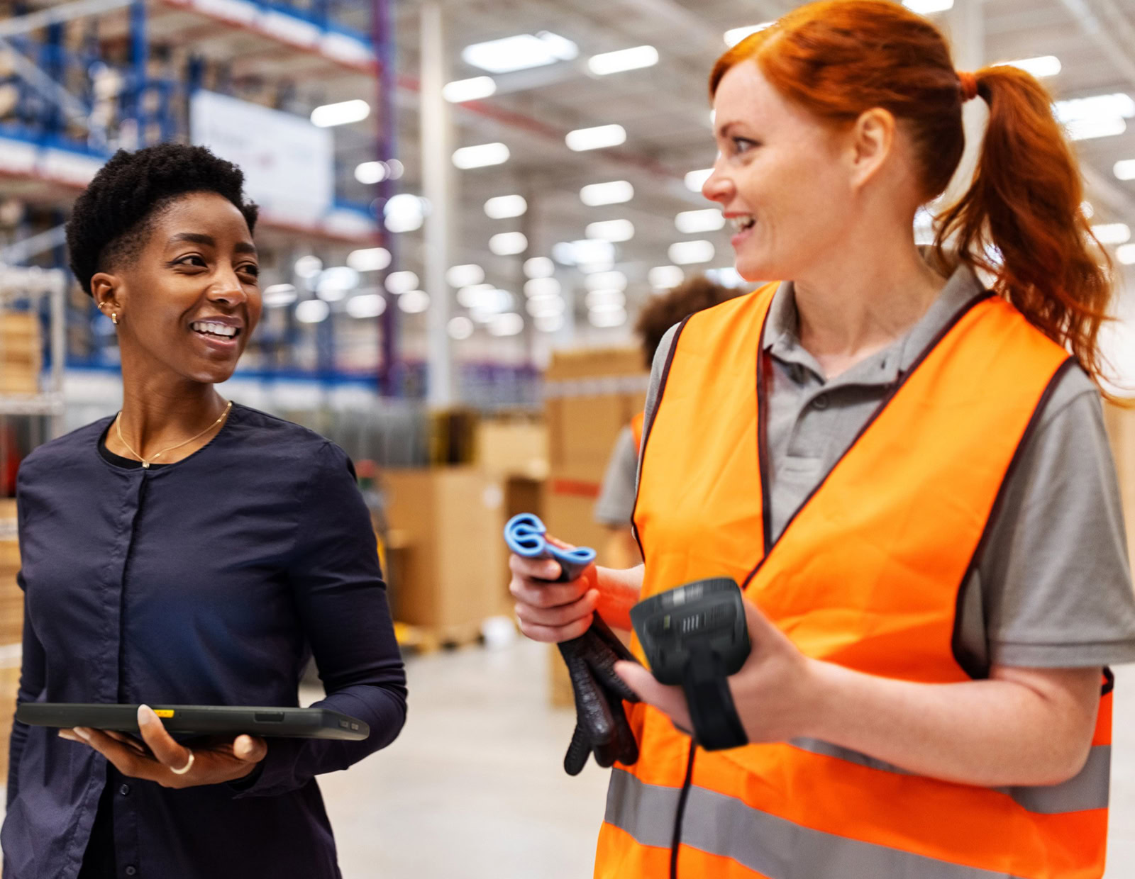 A read haired employee talks to a woman in a black shirt, both hold handheld ViziTrace devices using CheckMy.