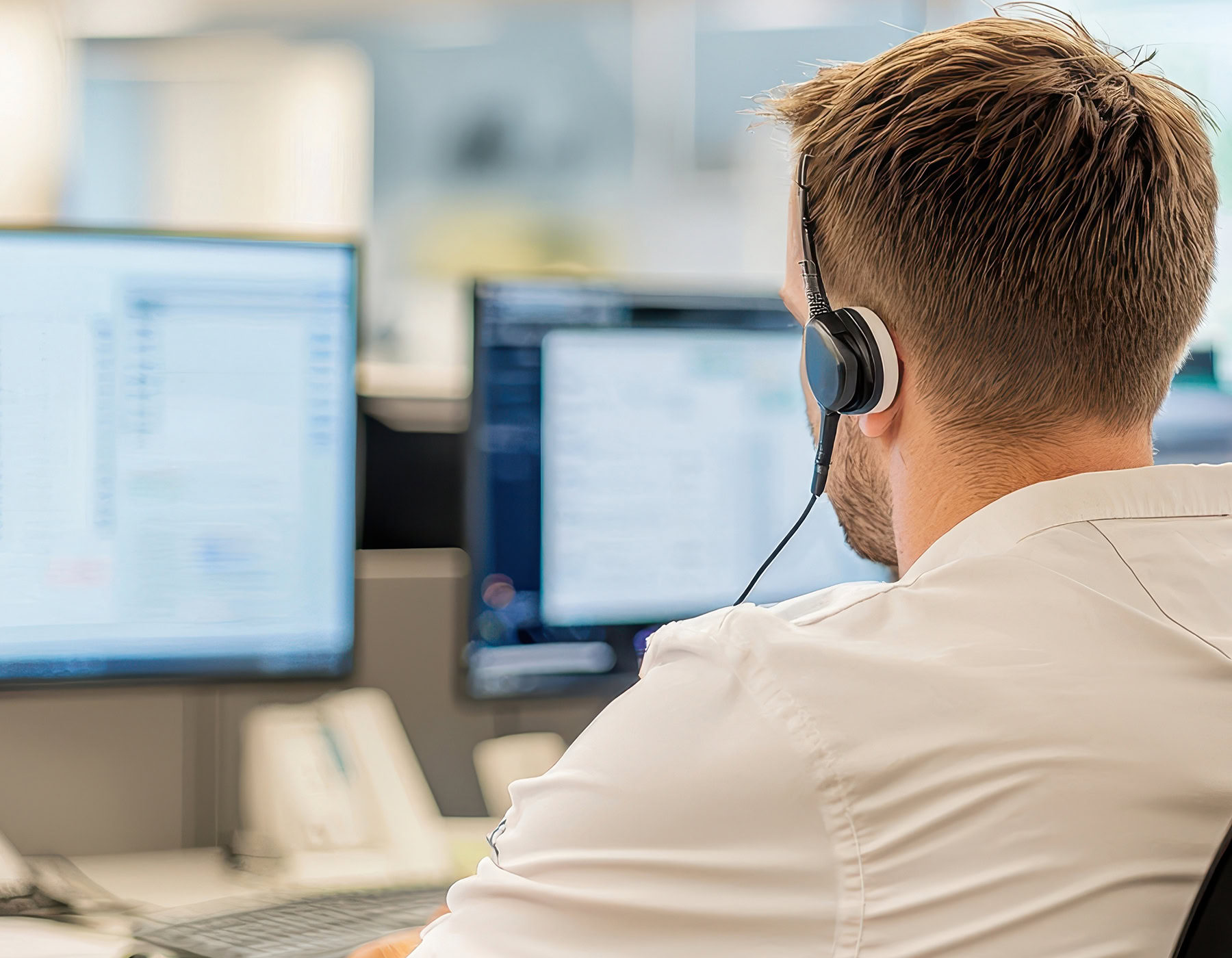 Specialist works on managed services, wearing a headset and watching monitors.