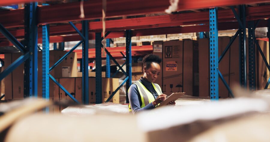 Worker performing a manual asset audit with a clipboard in a large warehouse