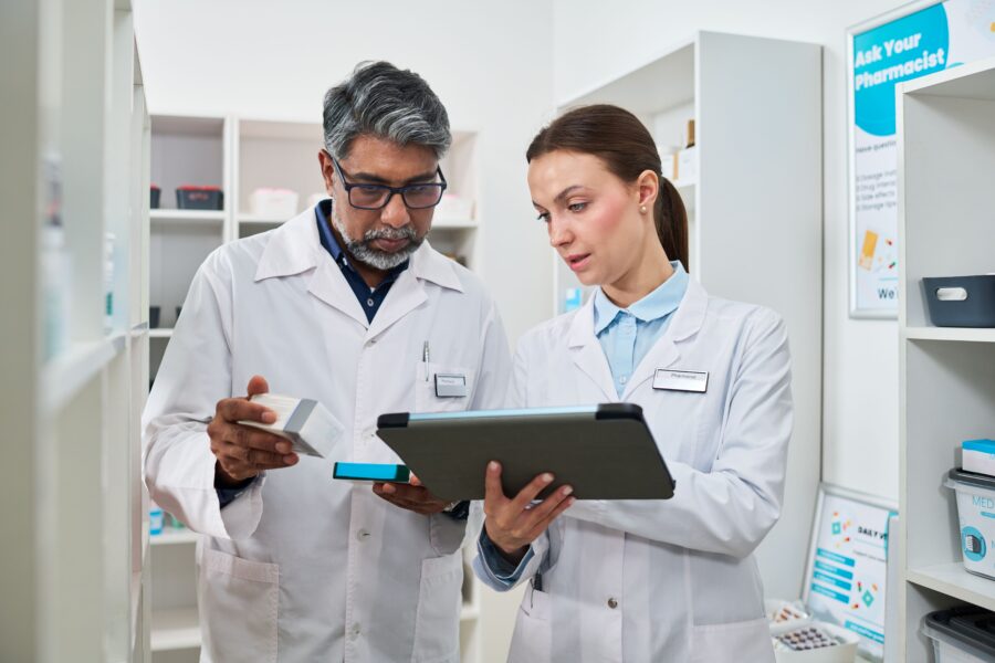 Two pharmacists comparing a product against a tablet, reviewing inventory together