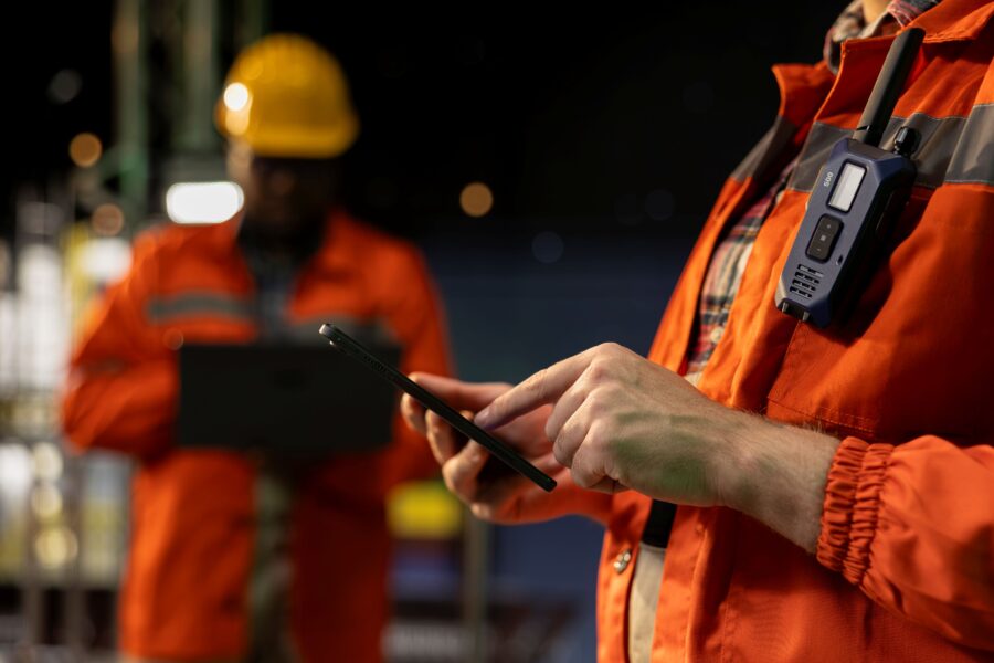 Worker checking an asset update on a phone with a colleague on a tablet behind, showing how asset tracking connects devices and people