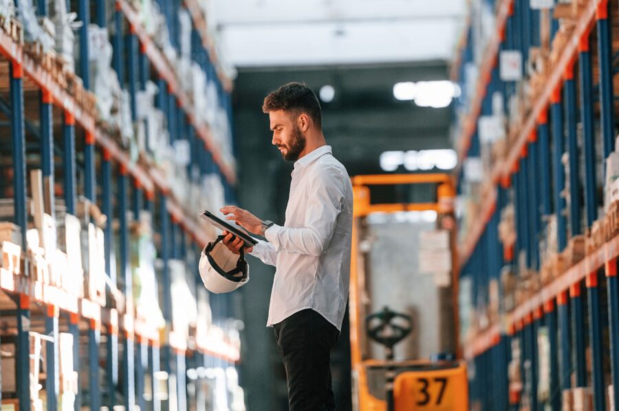 Warehouse worker calmly reviewing operations on a tablet, hard hat in hand